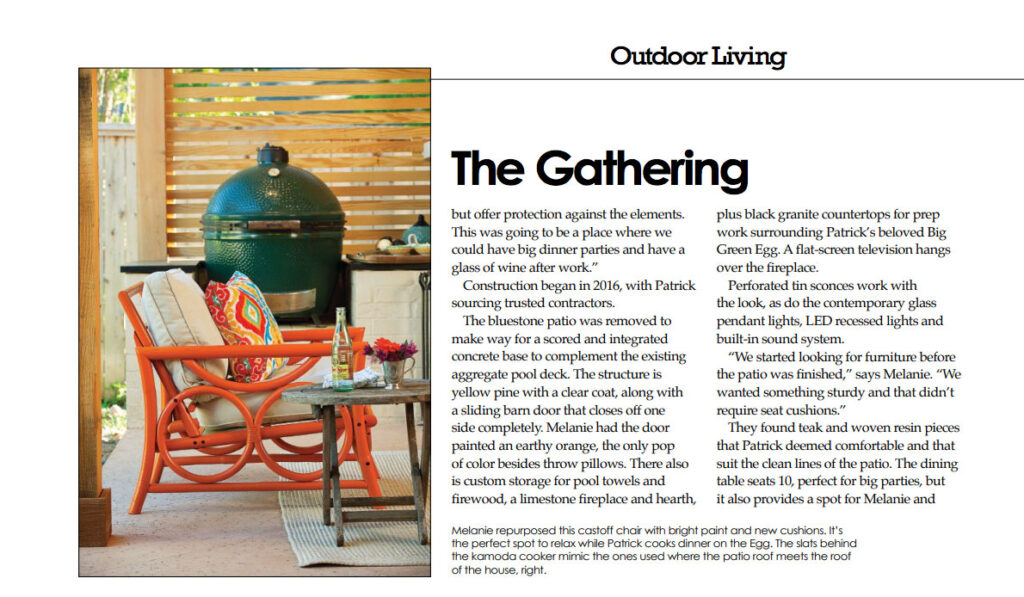 Outdoor patio seating area with an orange lounge chair, colorful cushions, side table, and green ceramic grill beside wood privacy slats.