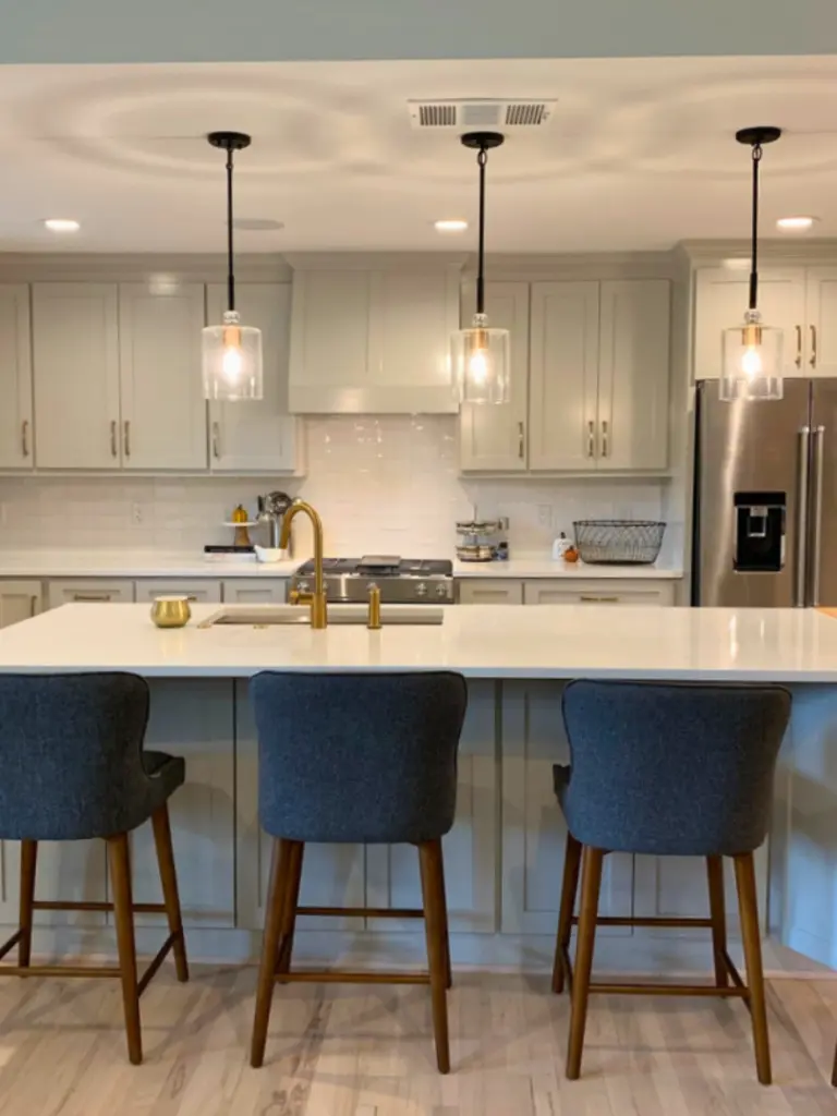 Modern kitchen with large island, pendant lighting, gold fixtures, and gray cabinetry