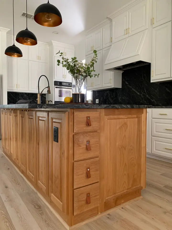 Luxury kitchen with natural wood island, black stone countertops, white cabinetry, and pendant lighting.
