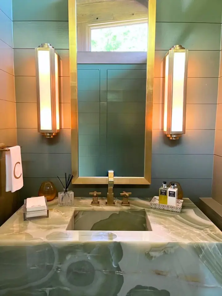 Modern powder bathroom with green stone sink, brass-framed mirror, and vertical wall sconces.