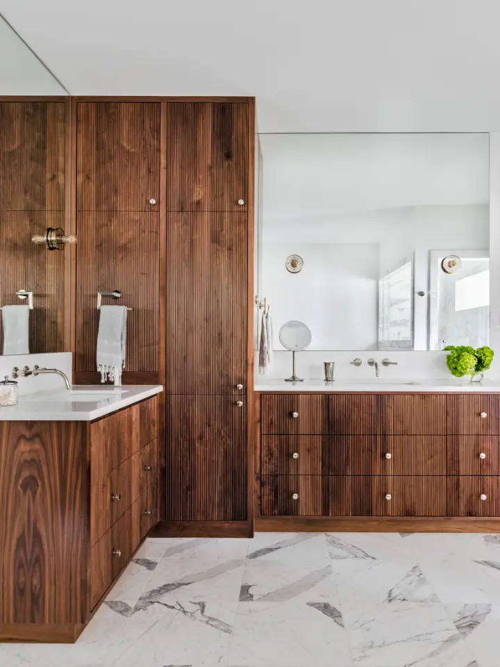 Modern bathroom with rich walnut cabinetry, integrated mirrors, marble flooring, and minimalist brass fixtures.