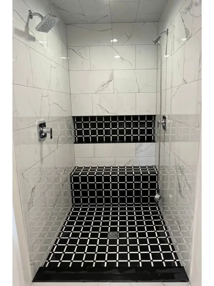 Modern walk-in shower with white marble tile, black geometric accent tile, and built-in bench seating.
