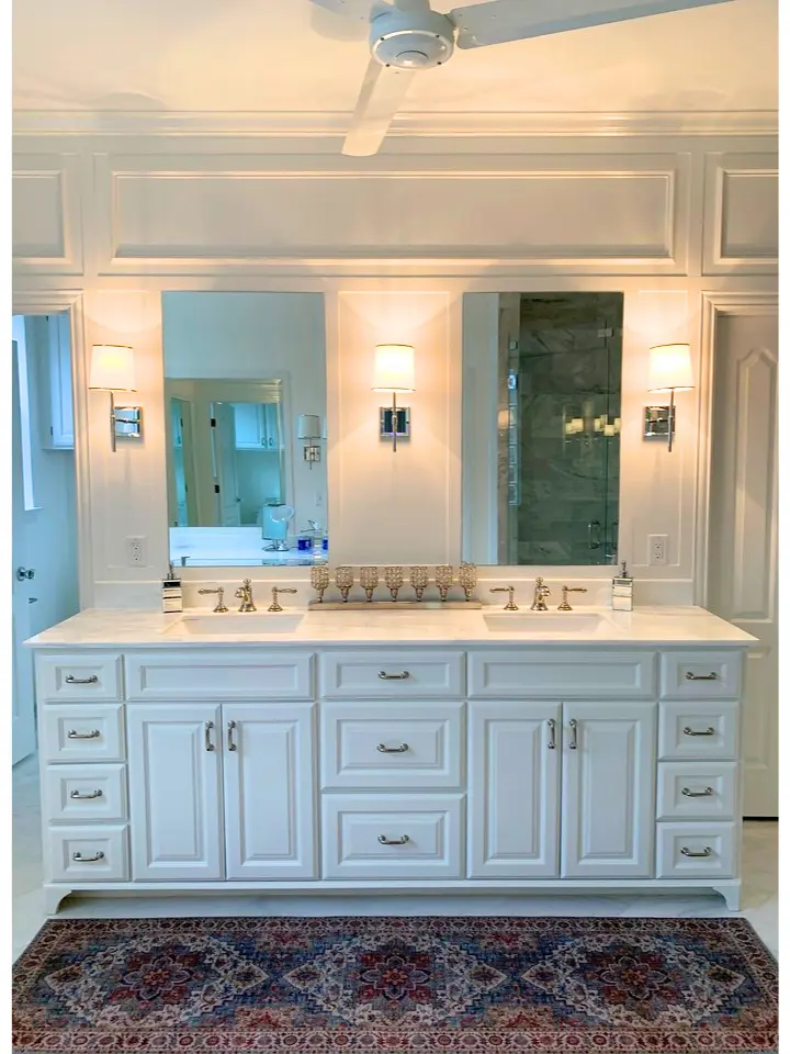 Elegant white double vanity bathroom with custom cabinetry, wall sconces, dual mirrors, and marble countertops.