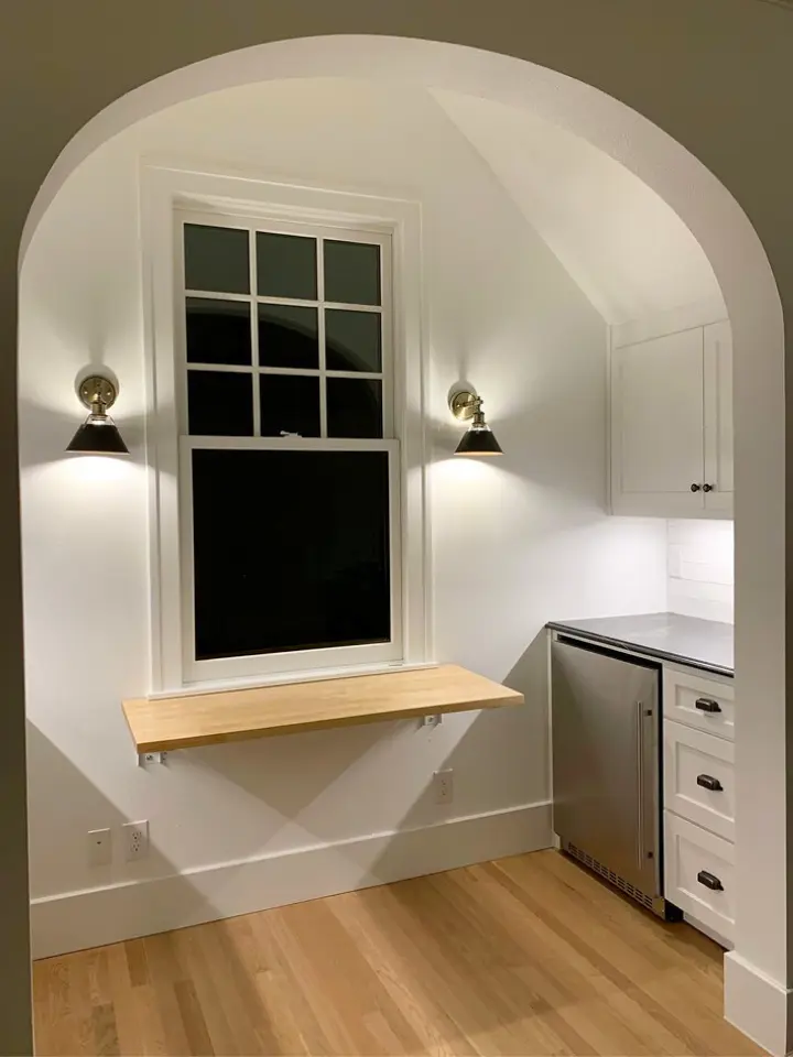 Built-in breakfast nook with floating wood shelf, arched entryway, black wall sconces, and custom white cabinetry.