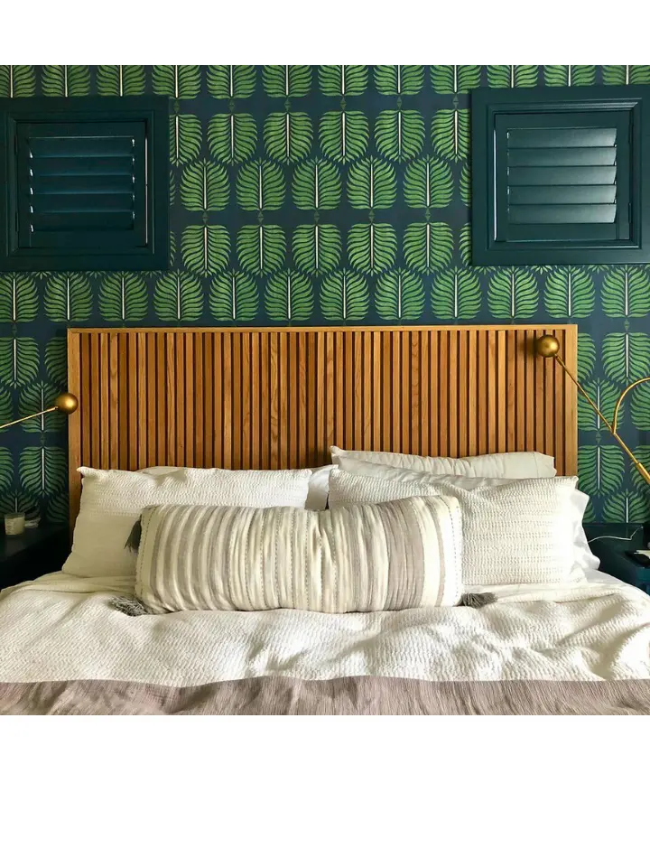 Modern bedroom with wood slat headboard, green patterned wallpaper, and brass accent lighting.