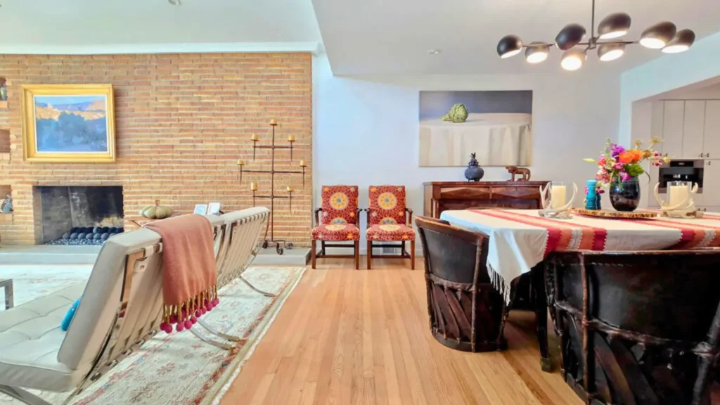 Mid-century modern dining and living room with brick fireplace wall, hardwood floors, colorful decor, and contemporary lighting.
