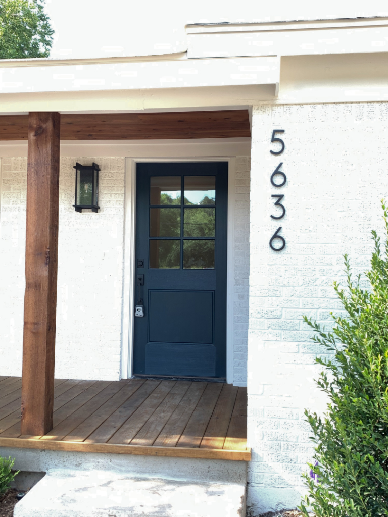 Modern home entrance with dark front door, wood porch accents, and contemporary house numbers