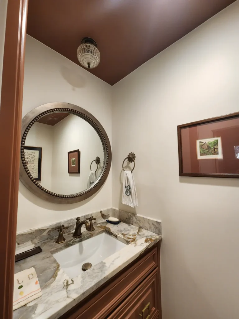 Elegant powder room with custom vanity, stone countertop, and decorative round mirror