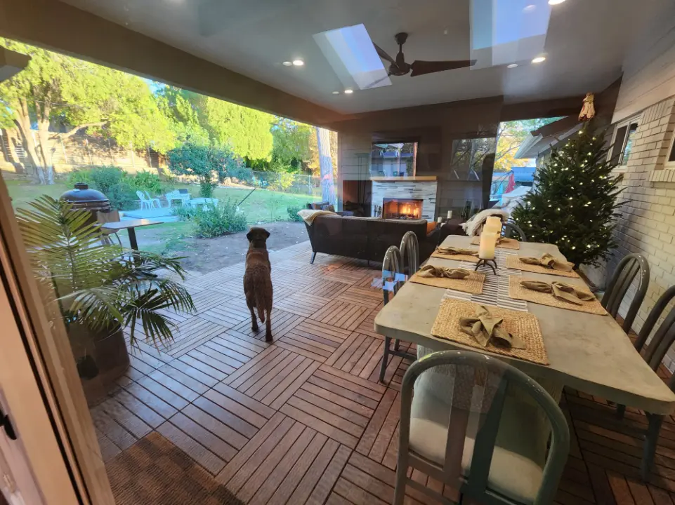 Covered outdoor patio with dining area, fireplace, skylights, and backyard view