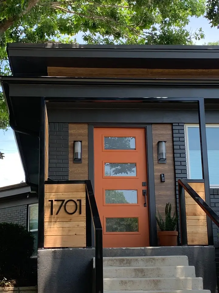 Modern home exterior with black brick facade, wood accents, and a bold orange front door.