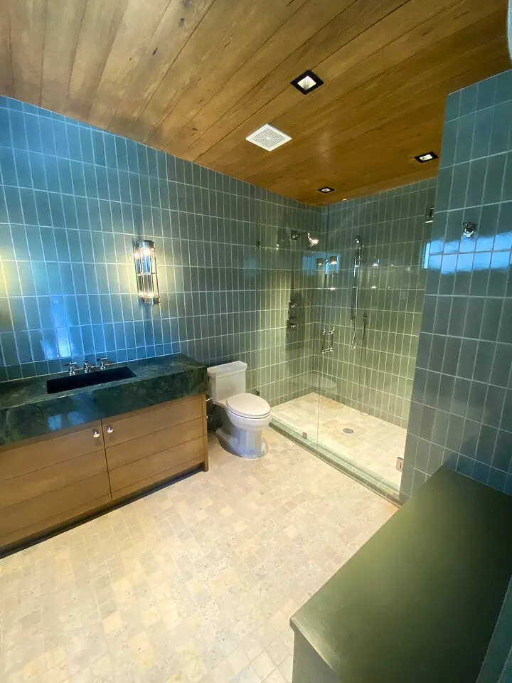 Modern bathroom with blue tile walls, wood ceiling, floating vanity, and frameless glass shower.
