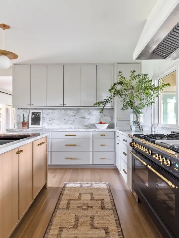Luxury kitchen with marble backsplash, brass hardware, natural wood island, and black professional gas range.