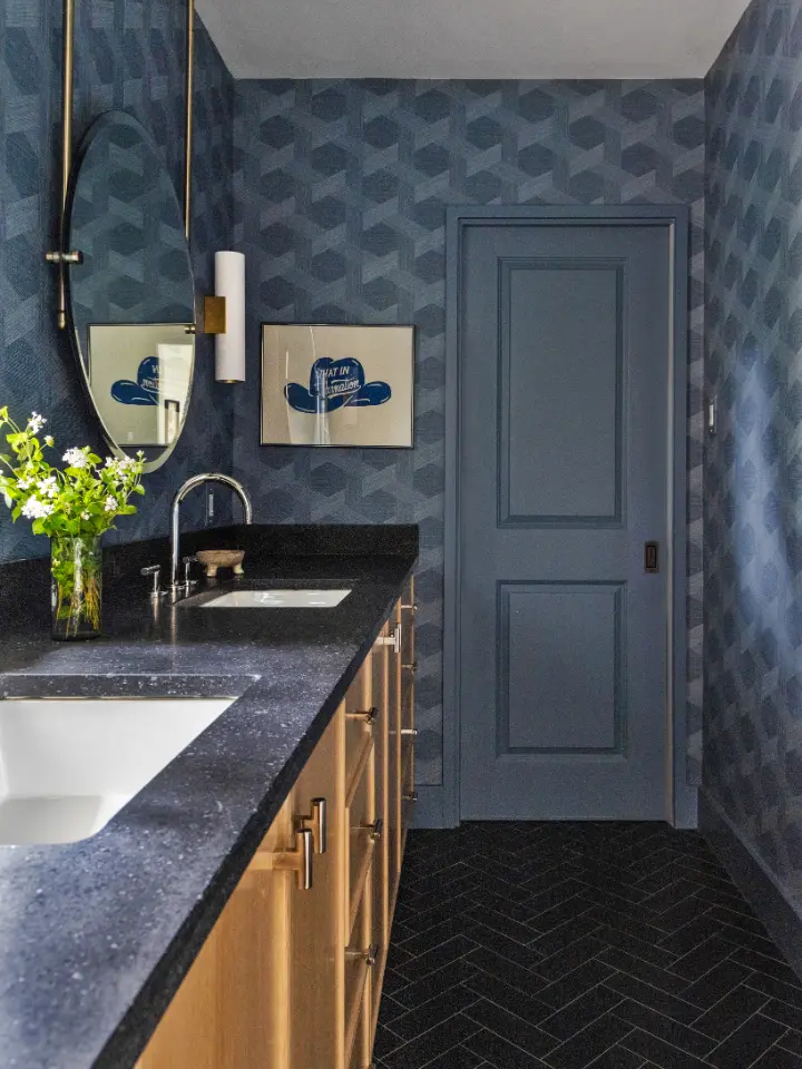Modern powder bathroom with dark blue geometric wallpaper, black countertop vanity, brass accents, and contemporary lighting.