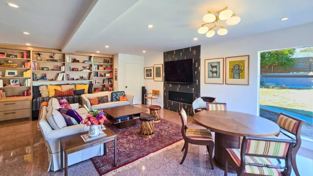 Modern open-concept living and dining room with built-in bookshelves, fireplace accent wall, colorful decor, and large windows.