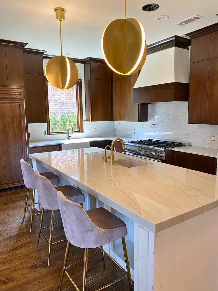 Luxury modern kitchen with waterfall quartz island, dark wood cabinetry, brass pendant lighting, and bar seating.
