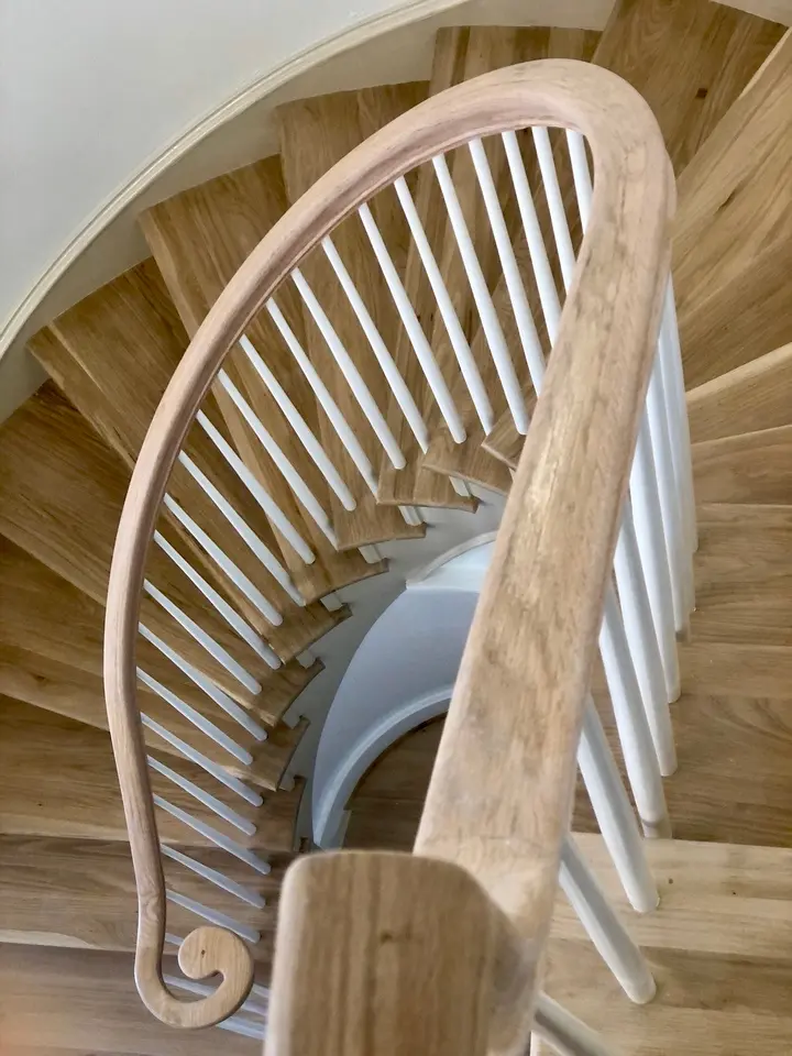 Curved wooden staircase with white balusters and natural oak treads viewed from above.