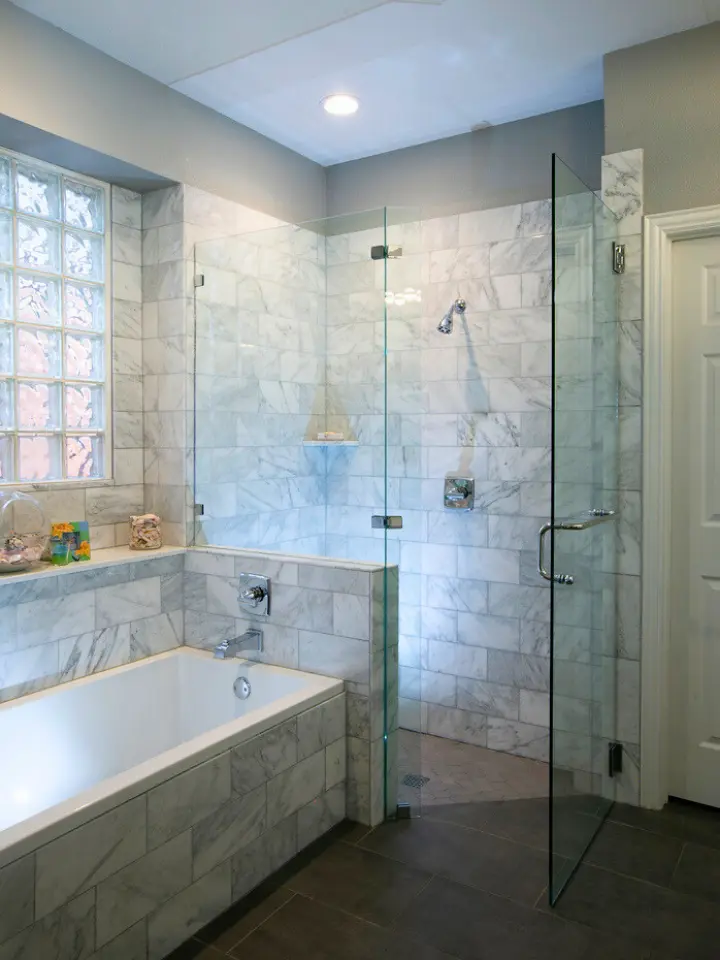Luxury bathroom with marble tile shower, frameless glass enclosure, soaking tub, and glass block window.