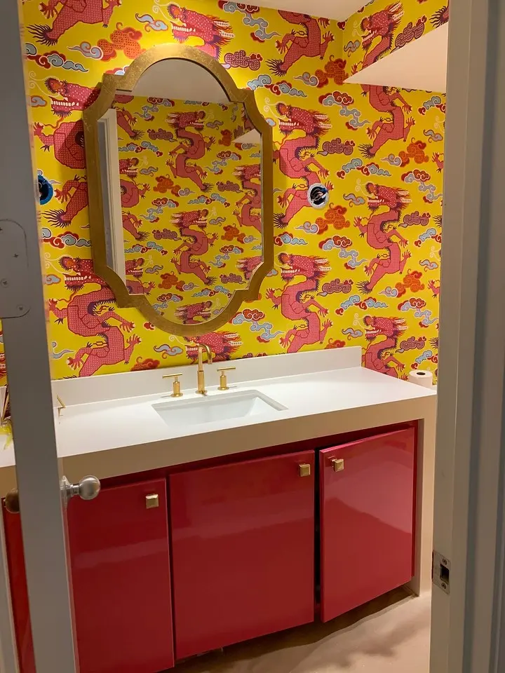 Bold powder room with colorful dragon wallpaper, red vanity cabinets, gold fixtures, and decorative mirror.