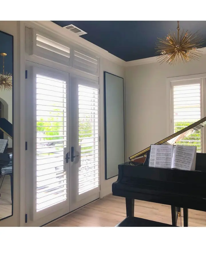 Elegant music room with black grand piano, blue ceiling, white plantation shutters, and modern chandelier.
