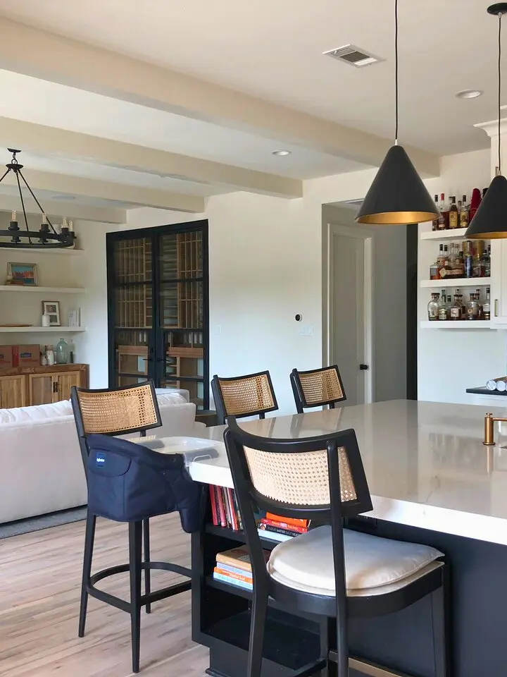 Modern open-concept kitchen with black island seating, woven bar stools, pendant lighting, and built-in shelving.