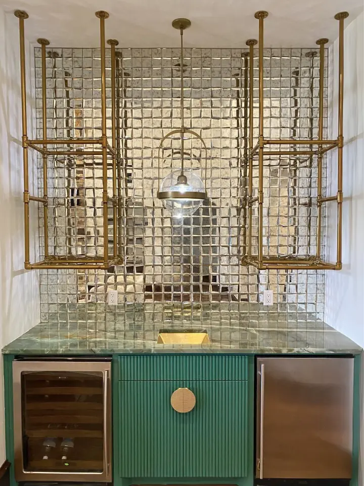 Luxury wet bar with mirrored tile backsplash, brass shelving, green cabinetry, and built-in beverage refrigerators.
