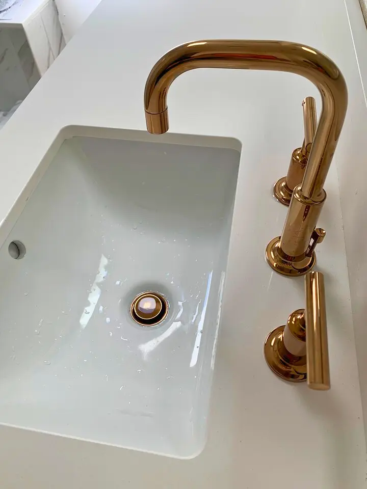 Close-up of a modern gold faucet and white sink with minimalist countertop design