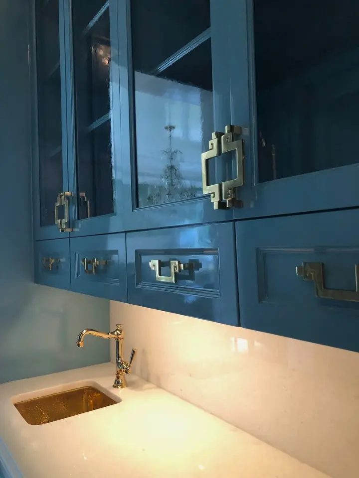 Custom blue built-in cabinetry with brass hardware, white countertop, and small brass sink.