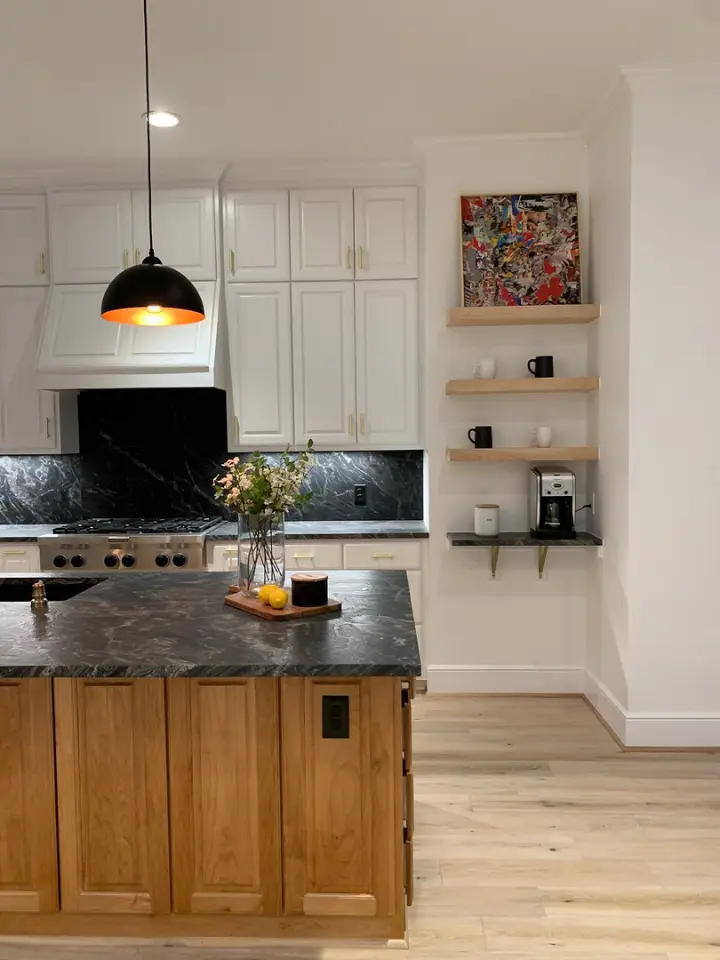 Modern kitchen with wood island cabinetry, black stone countertops, floating shelves, and pendant lighting.