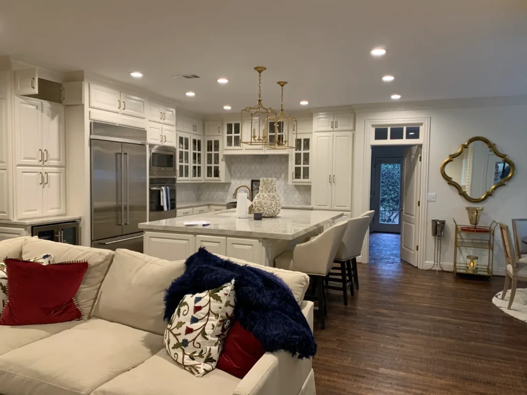 Luxury open-concept kitchen with white custom cabinetry, marble island countertops, stainless steel appliances, pendant lighting, and dark hardwood floors.