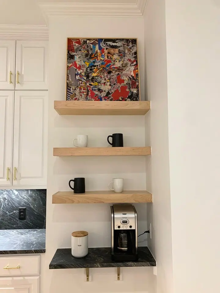 Modern coffee station with floating wood shelves, black stone countertop, espresso machine, and minimalist decor.