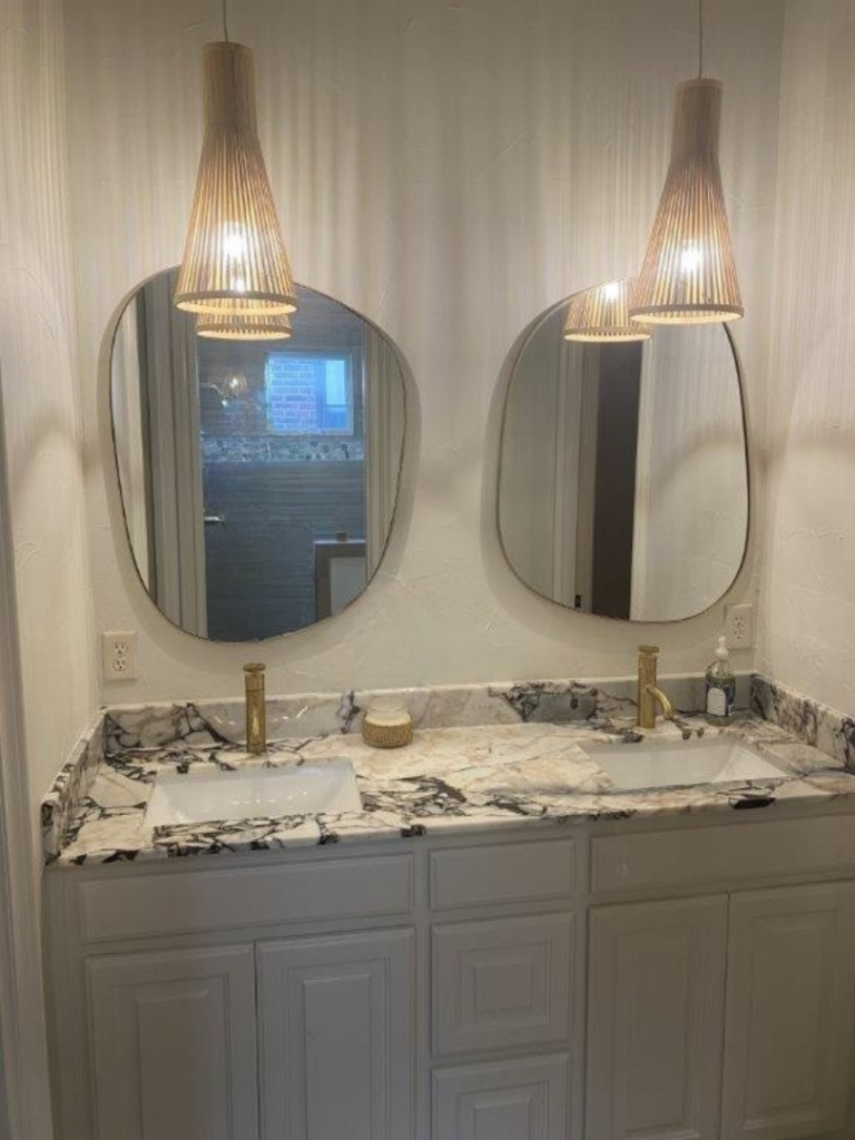 Custom double bathroom vanity with marble countertop, oval mirrors, and pendant lighting