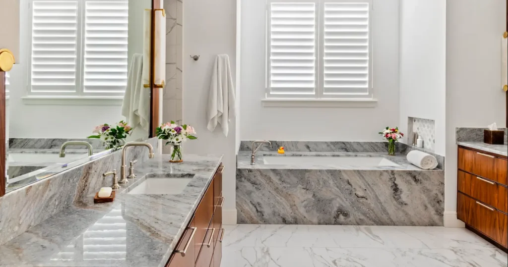Luxury bathroom with marble countertops, soaking tub, wood cabinetry, and bright natural light