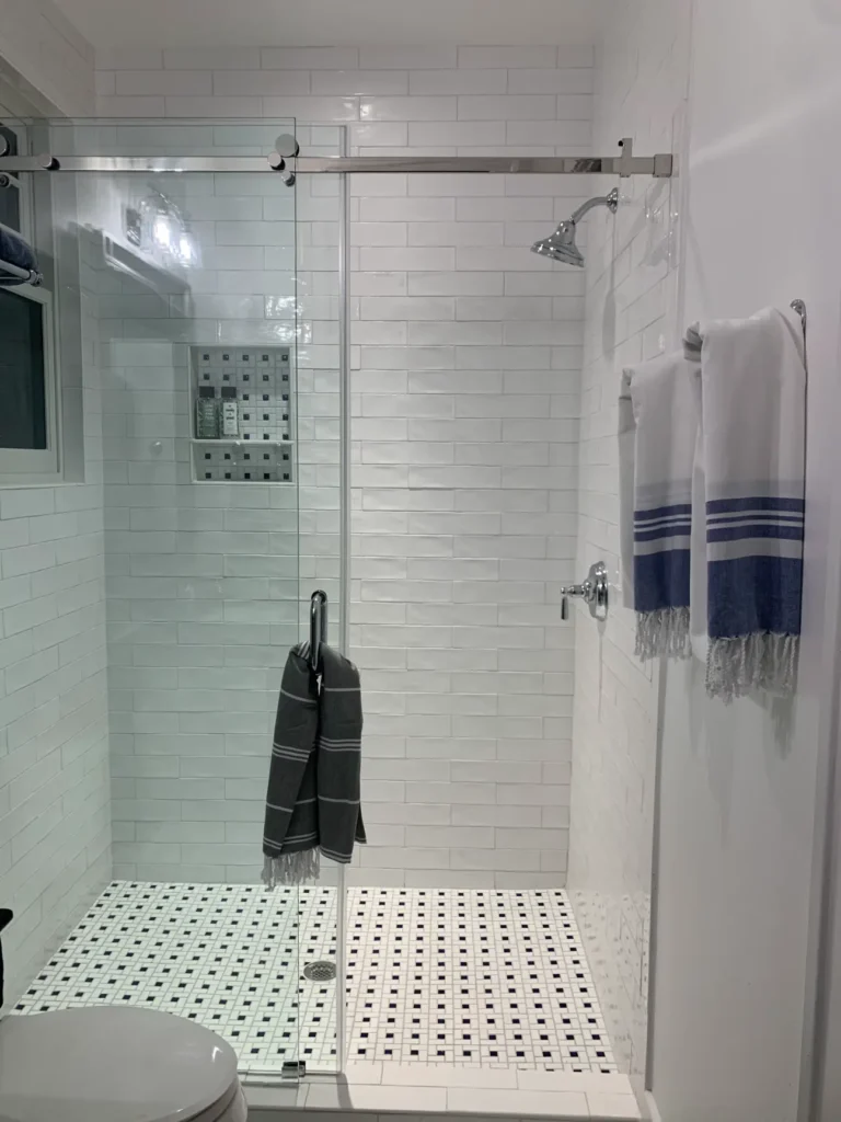 Modern walk-in shower with frameless glass enclosure, white subway tile walls, mosaic tile flooring, and chrome shower fixtures.