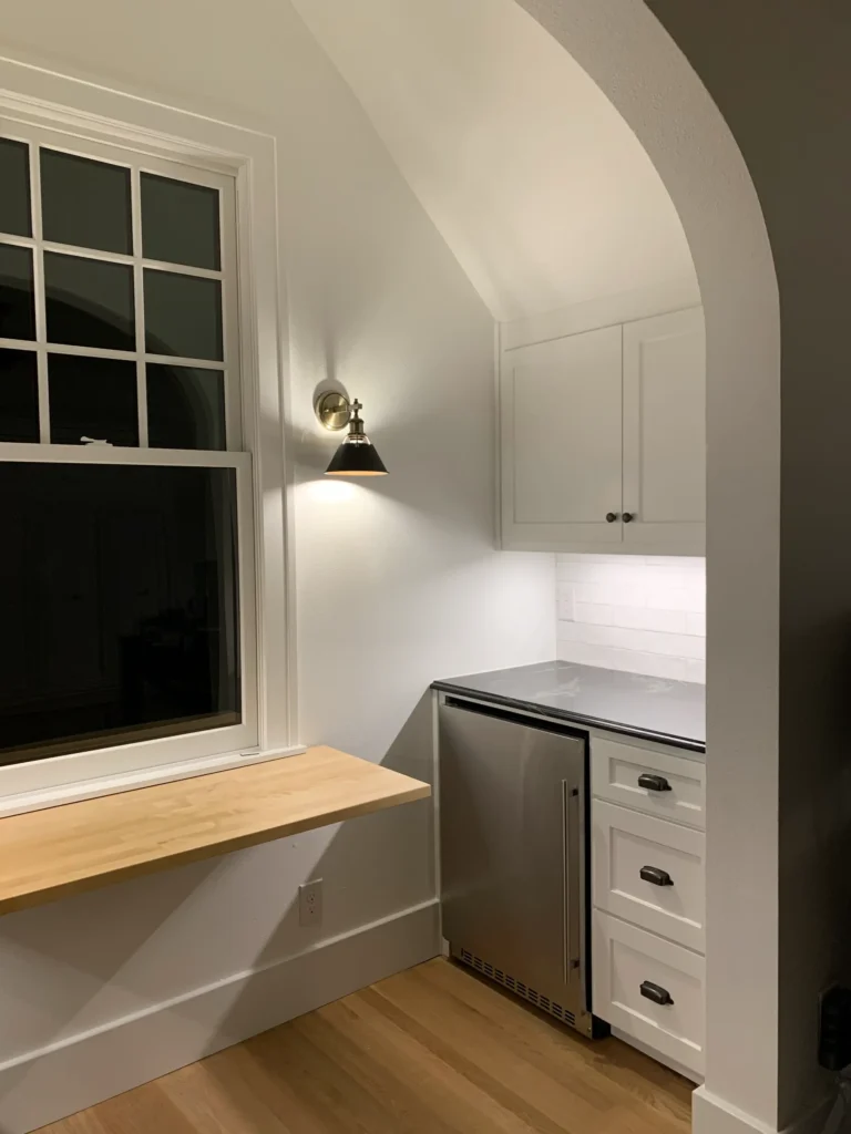 Modern wet bar with white cabinetry, mini refrigerator, subway tile backsplash, and arched entryway.