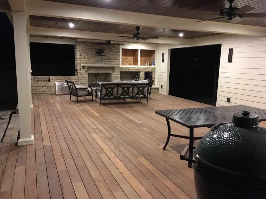 Covered outdoor deck with wood flooring, ceiling fans, stone fireplace, and lounge seating area