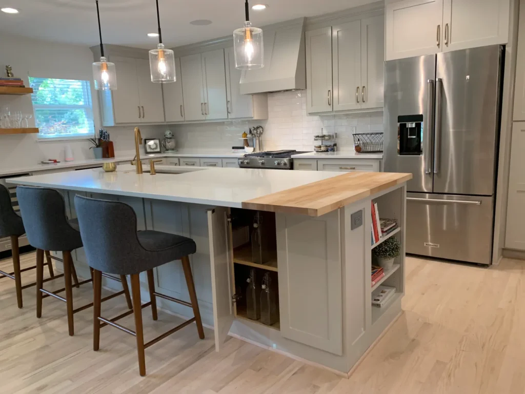 Modern custom kitchen with gray shaker cabinets, white quartz island countertop, stainless steel refrigerator, pendant lighting, and built-in shelving.