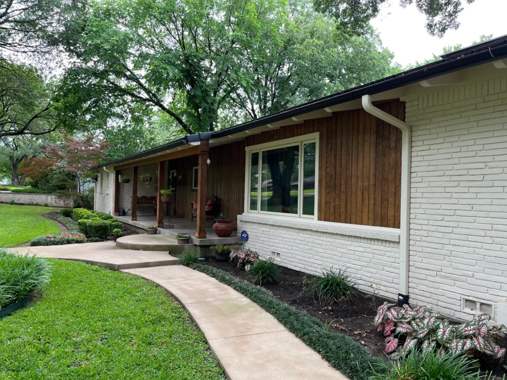Renovated front elevation featuring painted white brick, warm wood siding, updated landscaping, and a covered front porch