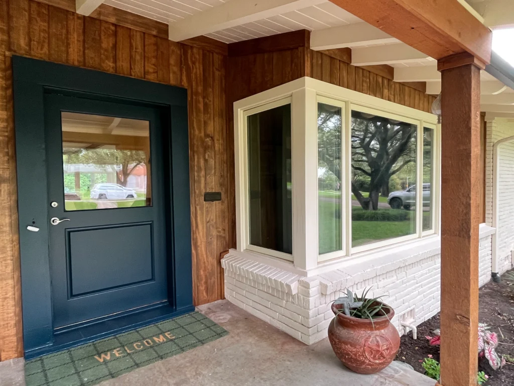 Renovated front porch with wood siding, dark entry door, modern windows, and exposed timber beams