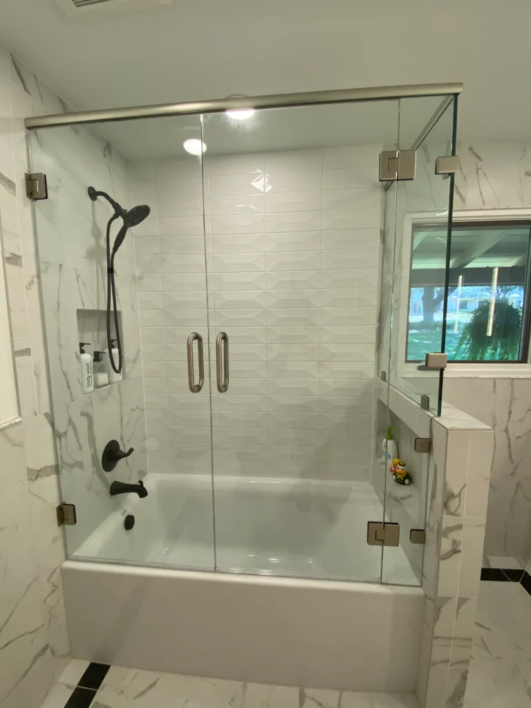 Modern glass enclosed shower and bathtub combination with marble tile walls and matte black fixtures