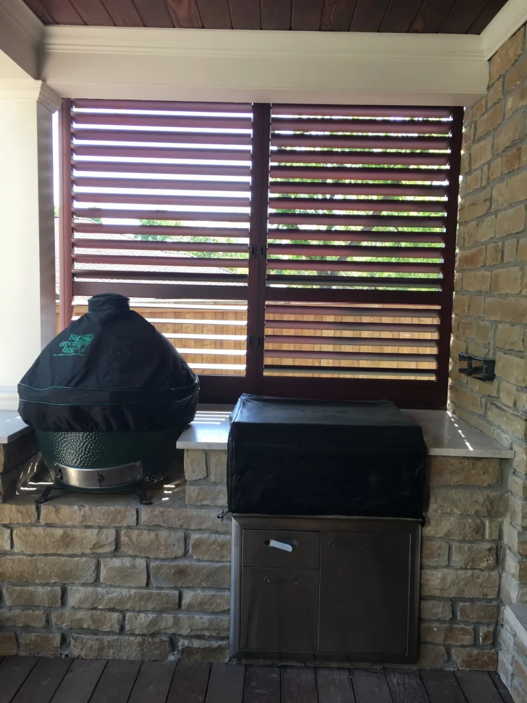 Built-in outdoor grilling station with stone surround and wood privacy screen on covered patio