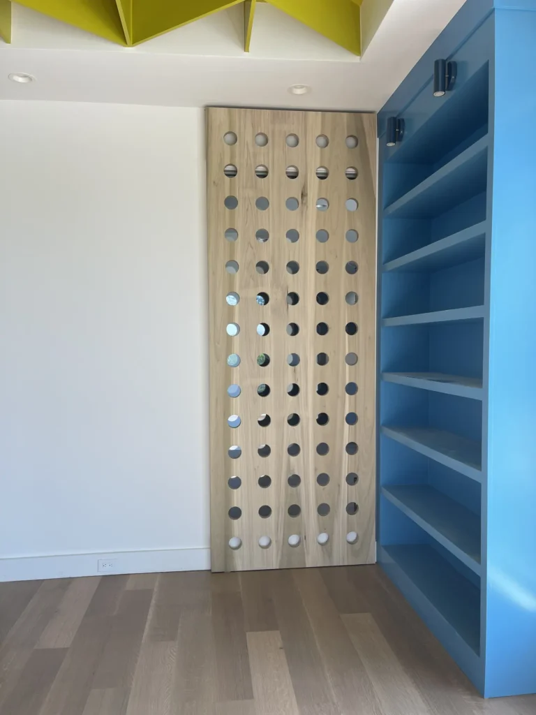 Modern custom wine storage wall with built-in bottle rack, blue shelving, and geometric ceiling accents.