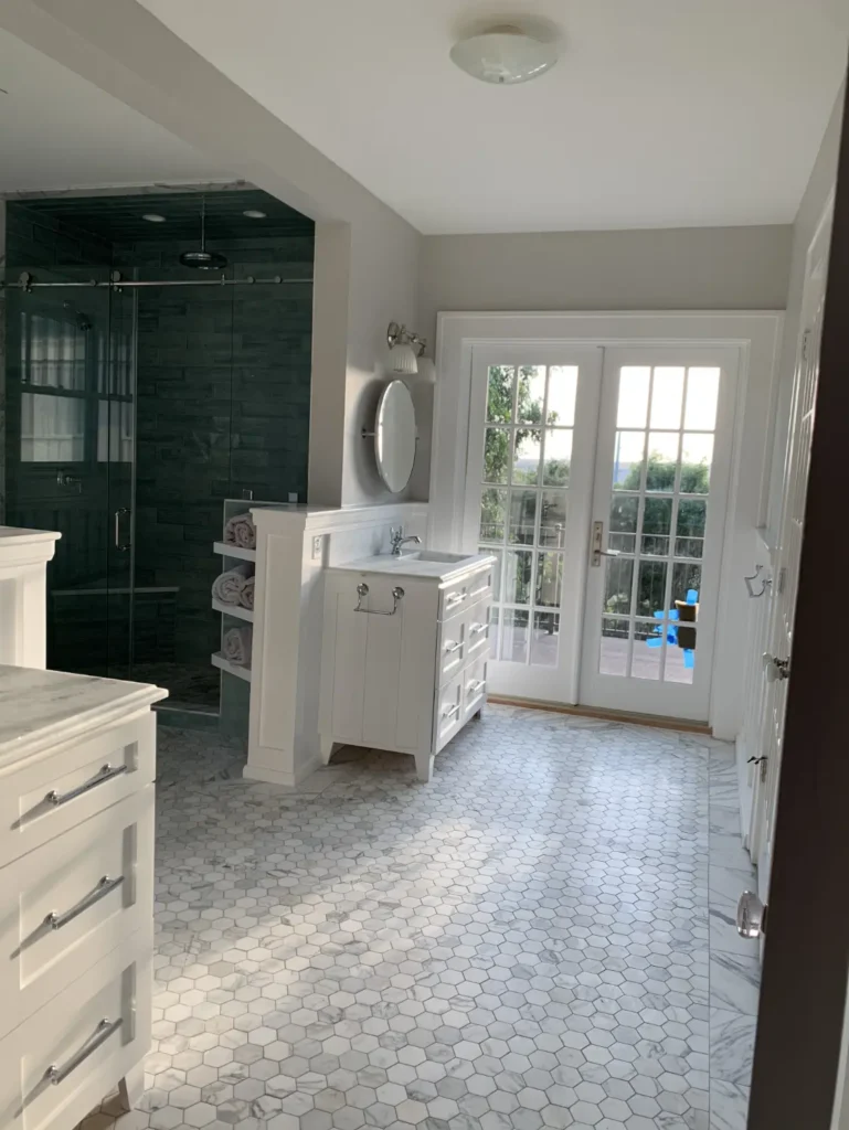 Luxury bathroom remodel with hexagon tile flooring, white vanity, frameless glass shower, and French doors leading outside.