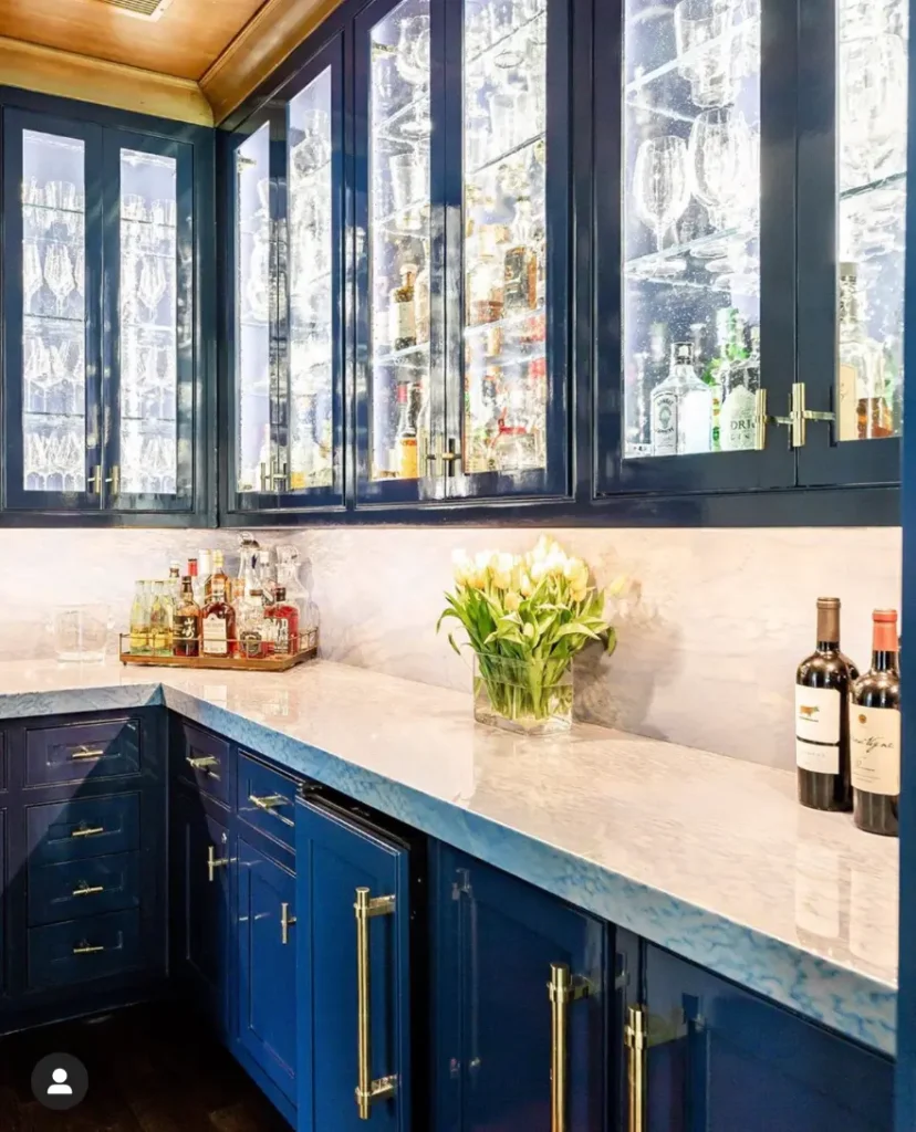 Luxury navy blue bar cabinetry with illuminated glass shelves, marble countertops, and brass hardware.