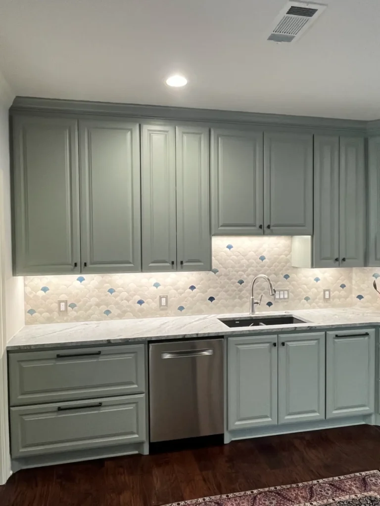 Kitchen remodel with gray custom cabinets, white quartz countertops, stainless steel dishwasher, and decorative scalloped tile backsplash.