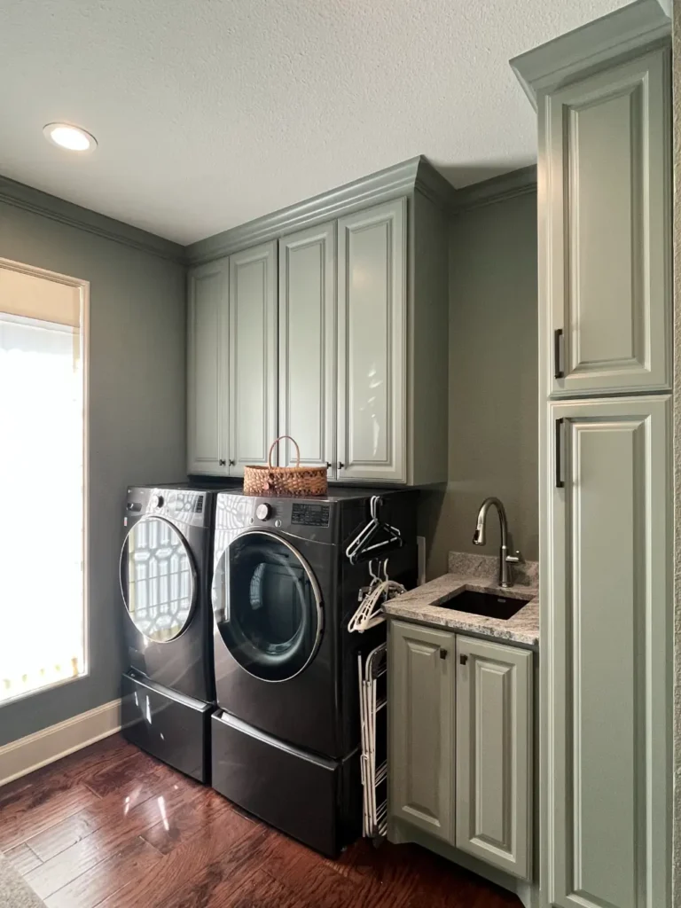 Custom laundry room with built-in cabinetry, stacked washer and dryer, utility sink, and hardwood flooring