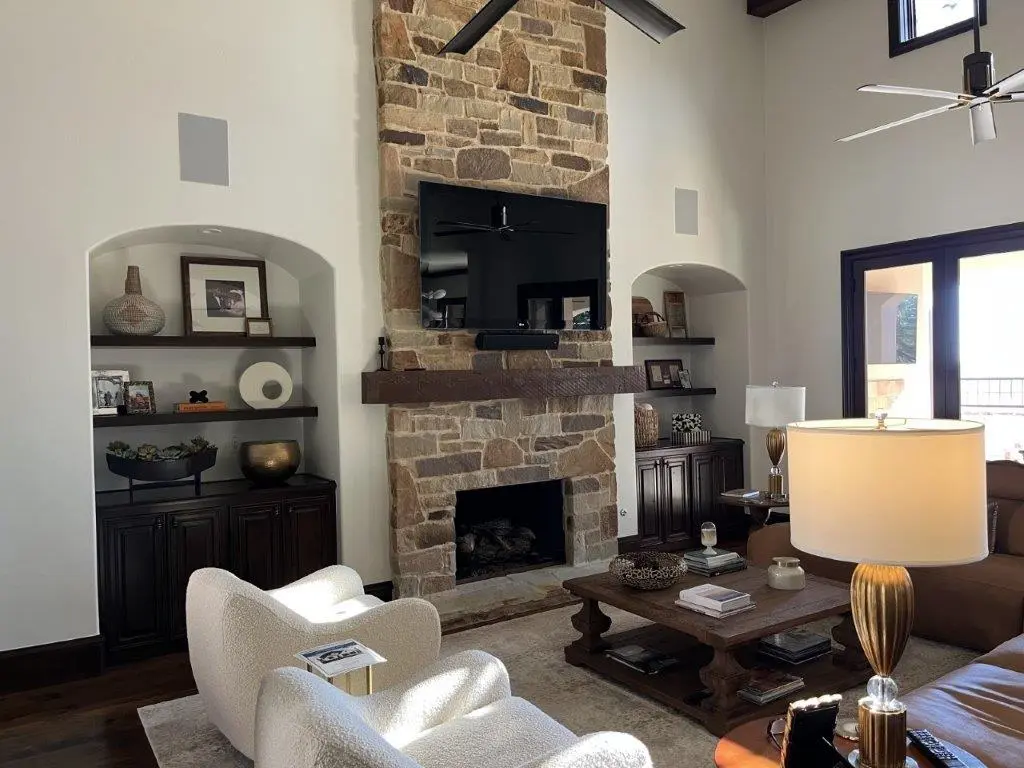 Vaulted living room with stone fireplace, custom built-ins, leather seating, and modern ceiling fans.