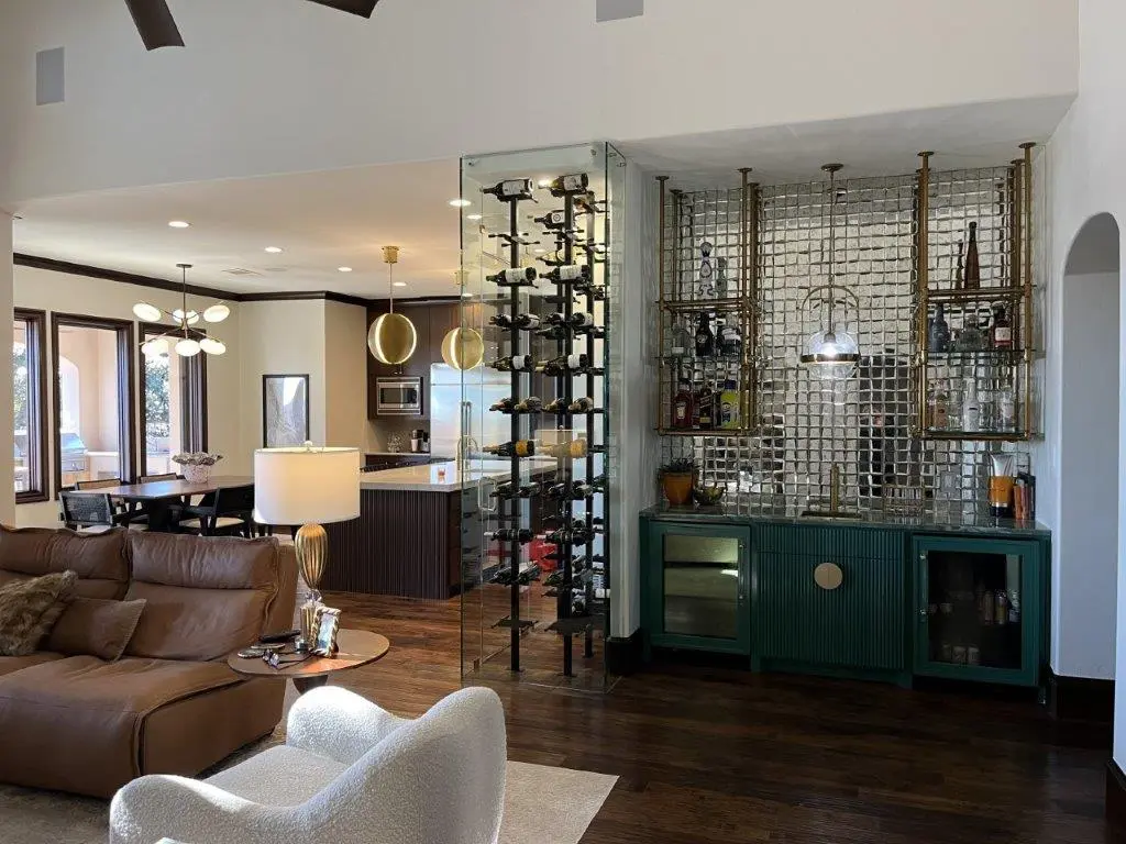 Luxury open-concept living room with glass wine display, custom home bar, and modern kitchen in the background.