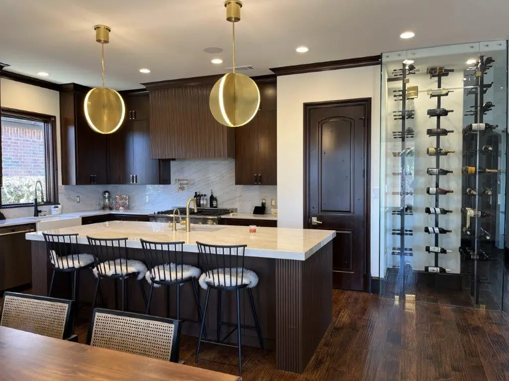 Luxury kitchen with dark wood cabinetry, oversized marble island, brass pendant lights, and modern bar seating.