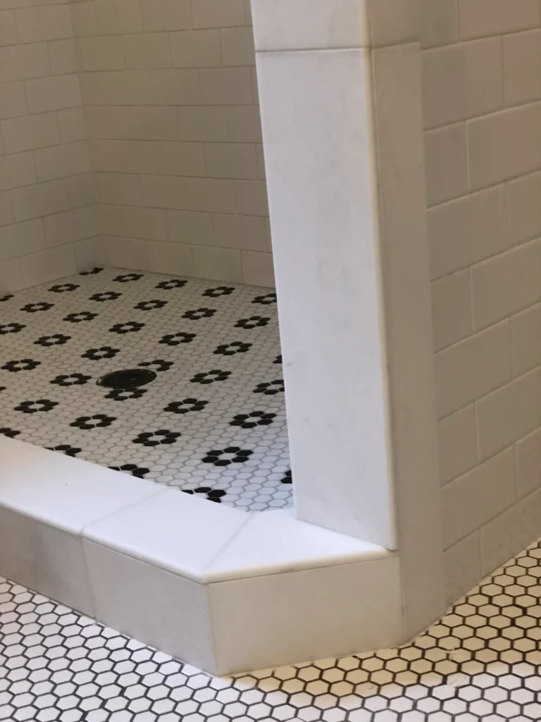 Custom walk-in shower with white subway tile walls, black floral mosaic tile flooring, and hexagon tile accents.