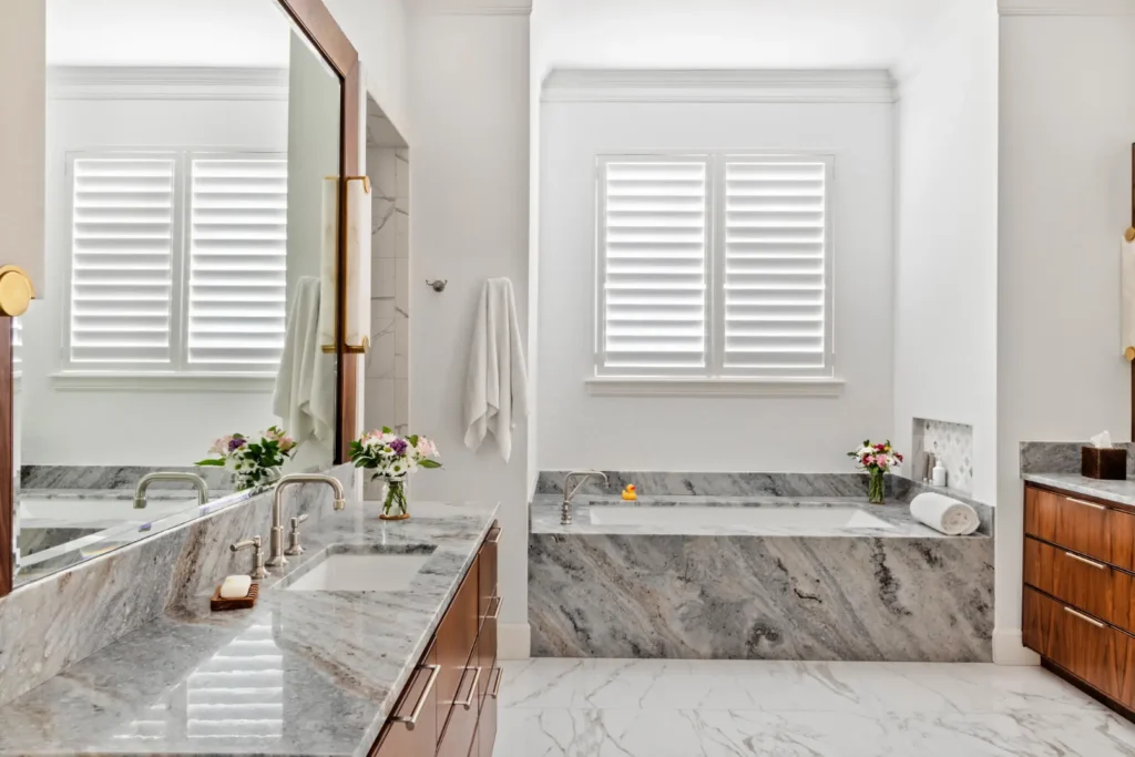 Luxury bathroom with marble countertops, soaking tub, wood cabinetry, and bright natural light